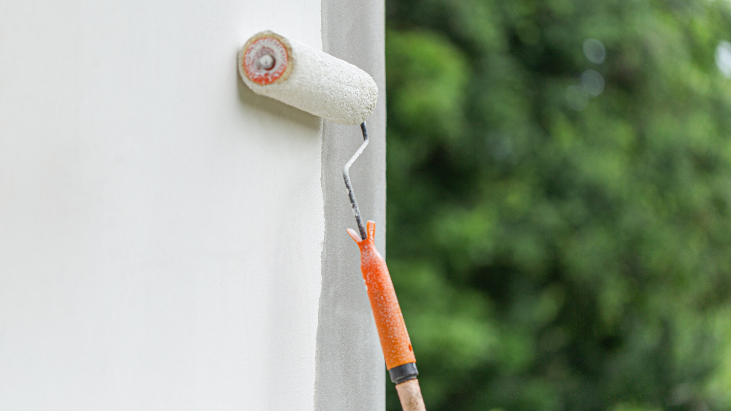 Paint roller applying fresh coat to exterior building wall
